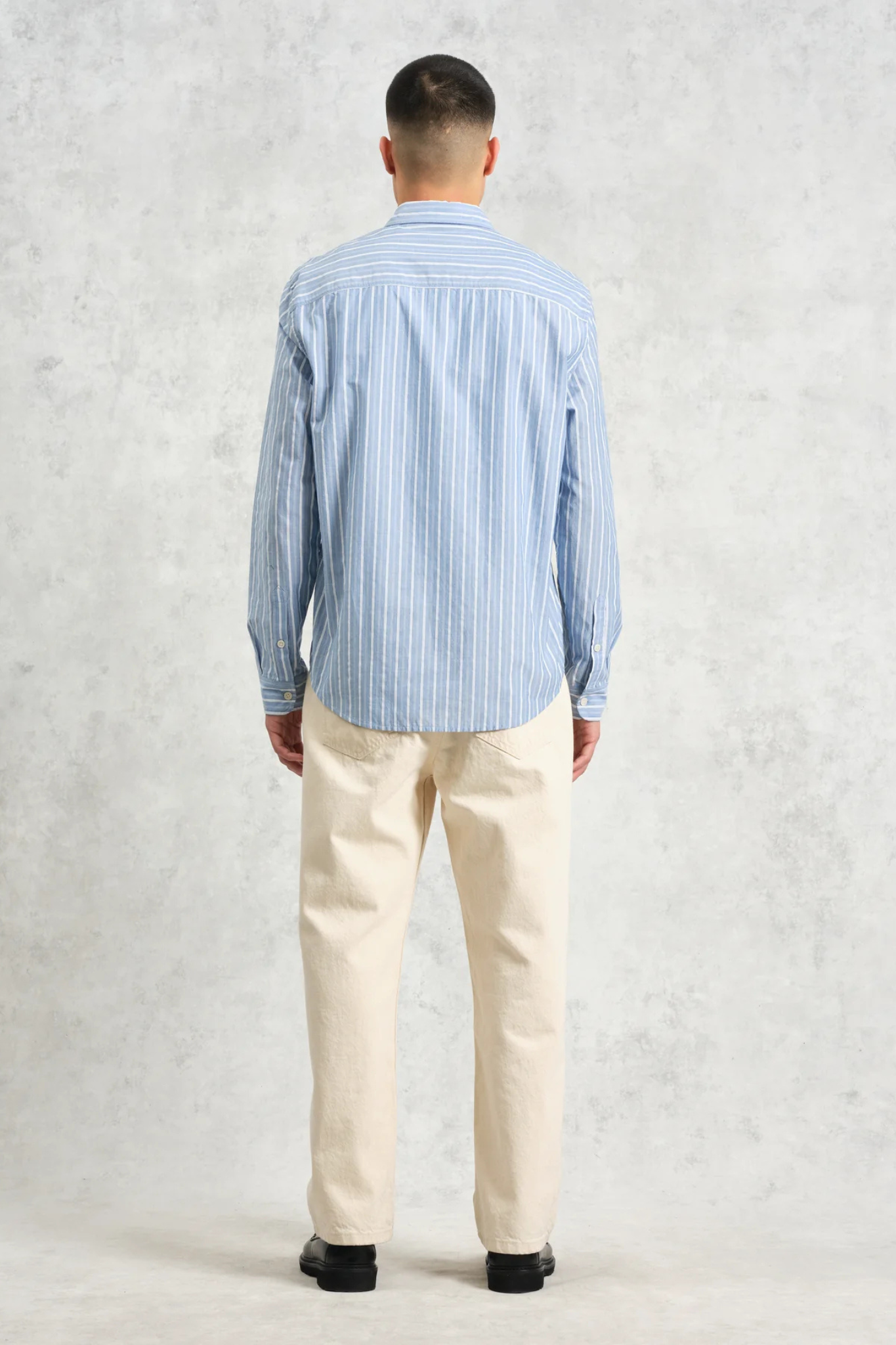 Model wearing the Wax London rove poplin stripe shirt in blue. Back view