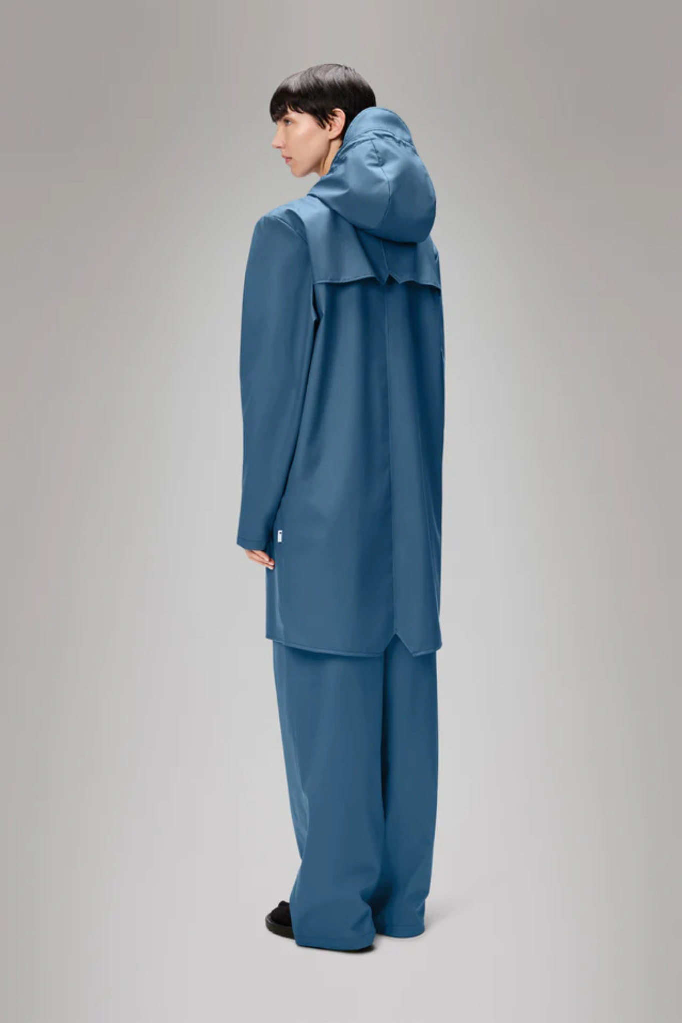 Model wearing the Rains long jacket W3 in blue. Back view