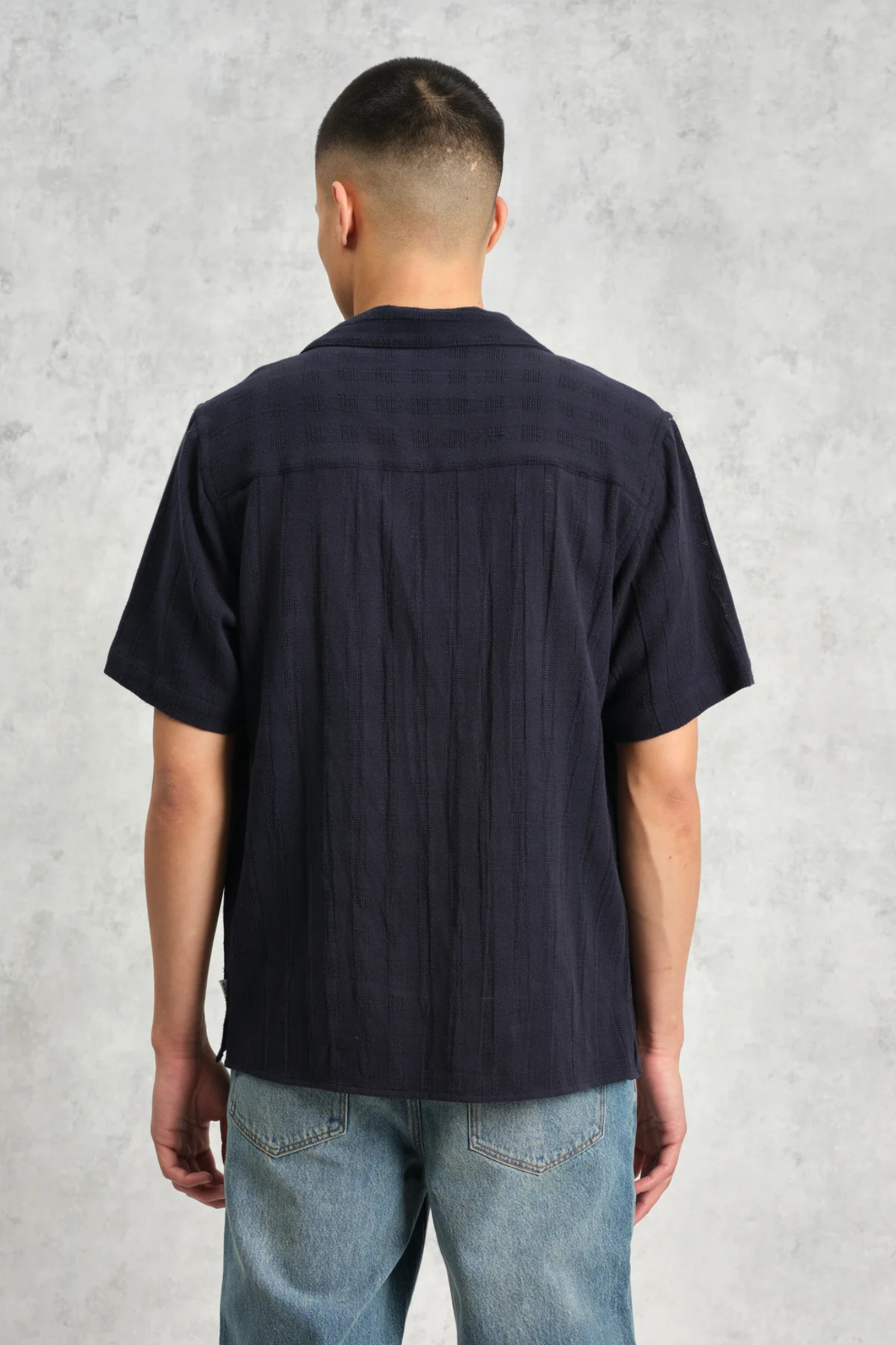 Model wearing the Wax London didcot box open weave grid shirt in navy. Back view