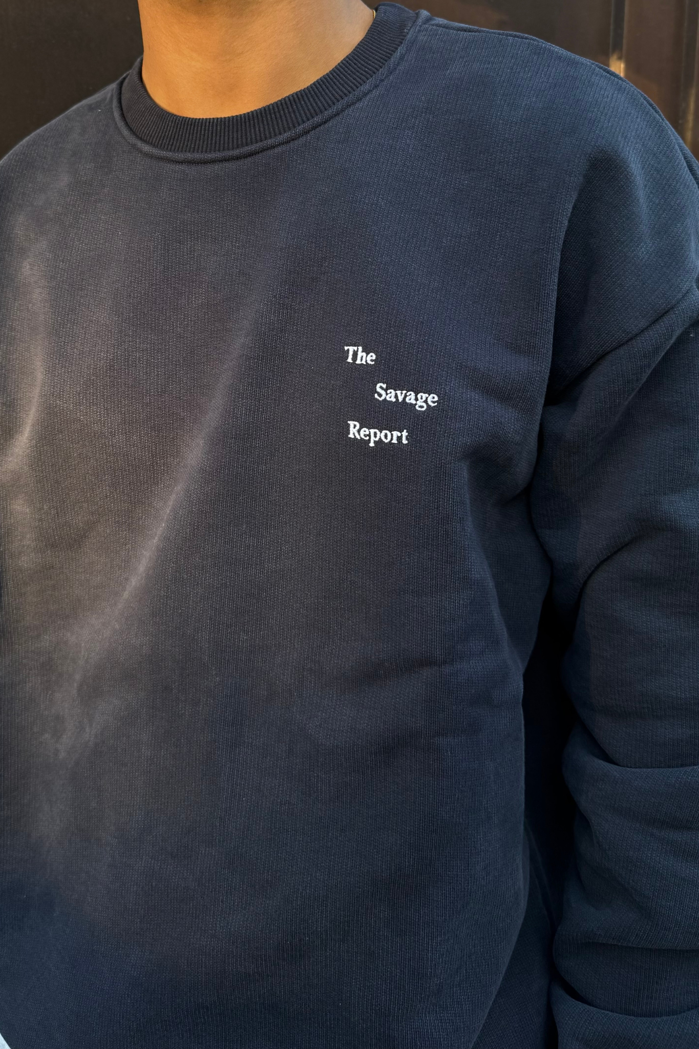 Model wearing The Savage Report wave logo crewneck in navy. Front view