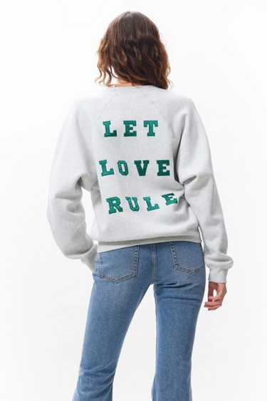 Model wearing the Catwalk Junkie grey graphic sweater with letters in green. Back view