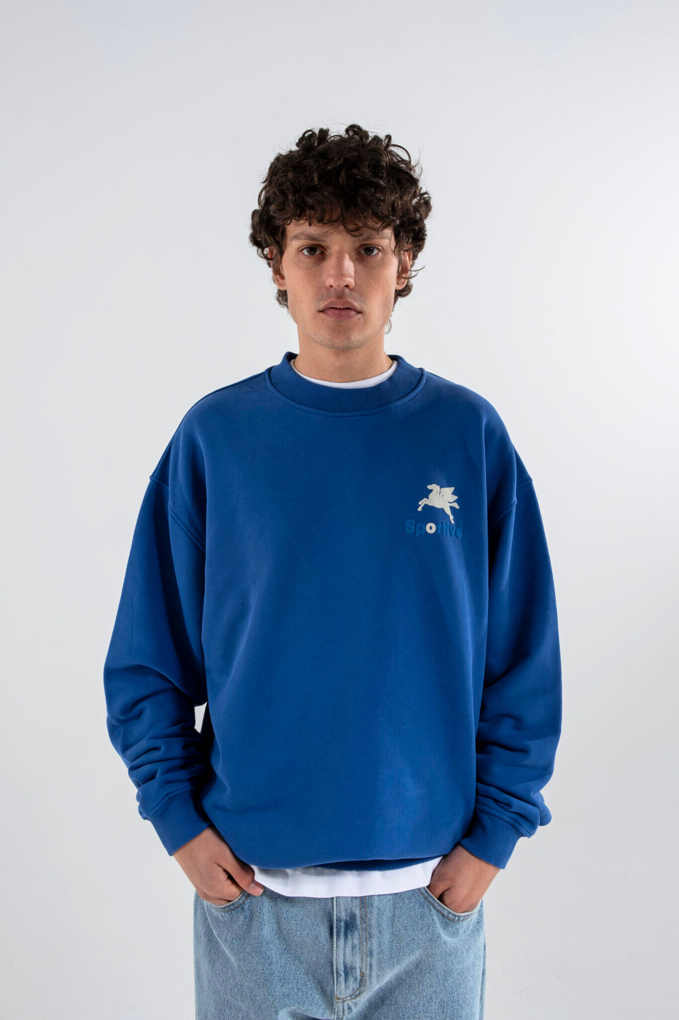 Model wearing the Goodies Sportive crewneck sweater in blue and logo in white. Front view