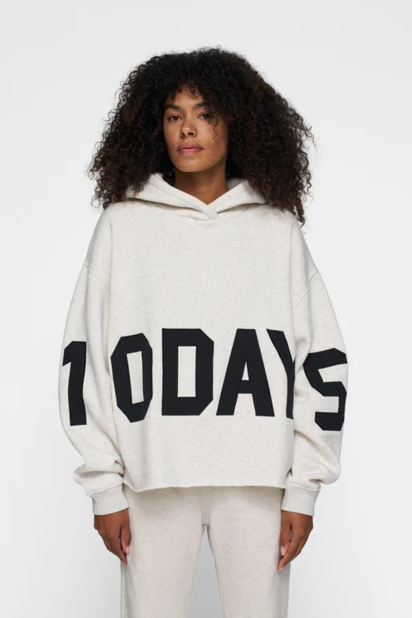 Model wearing the 10DAYS statement logo hoodie in soft white melee. Front view