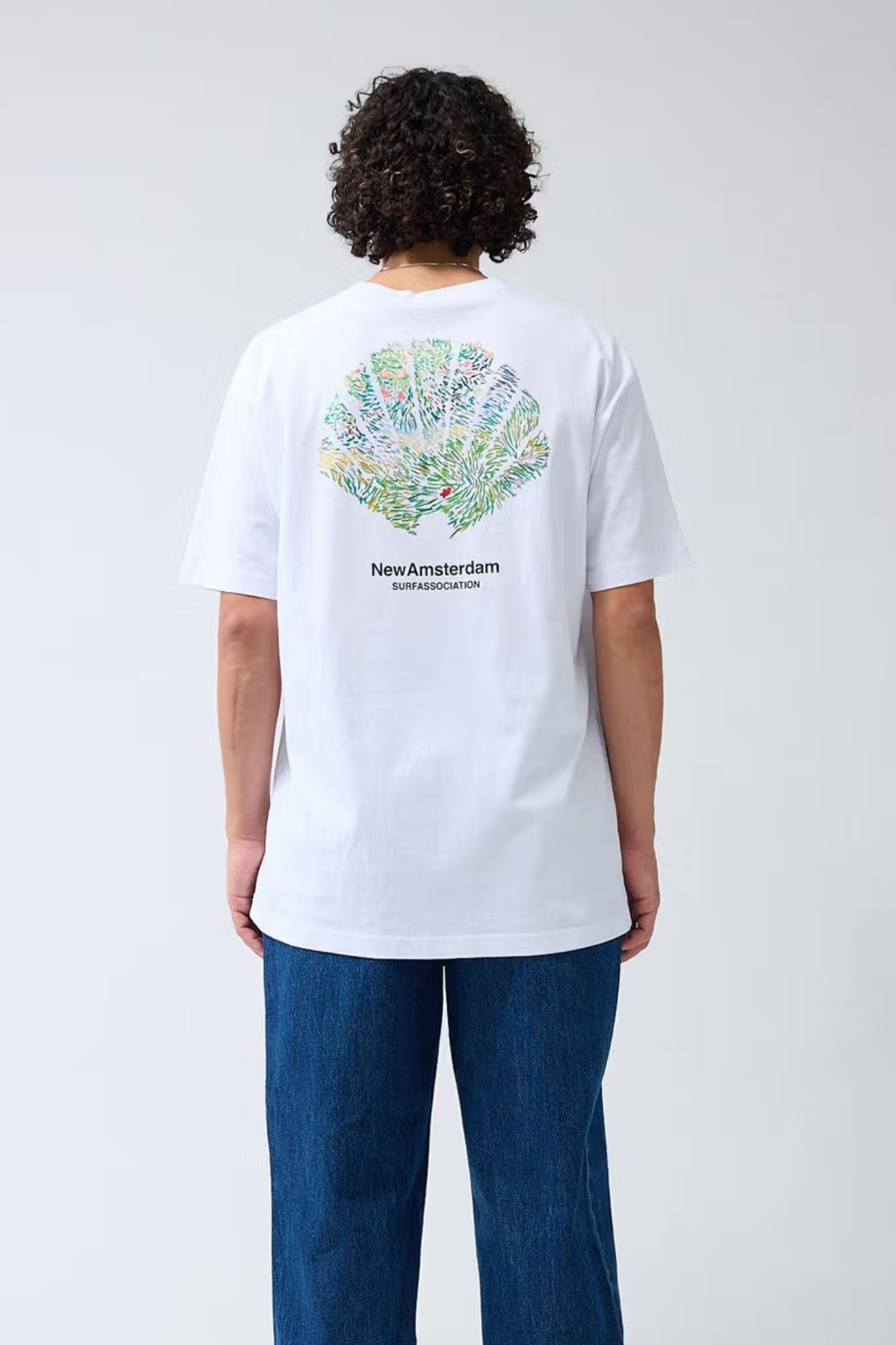 Model wearing the New Amsterdam tall grass white t-shirt with photo on the back and logo in black. Back view