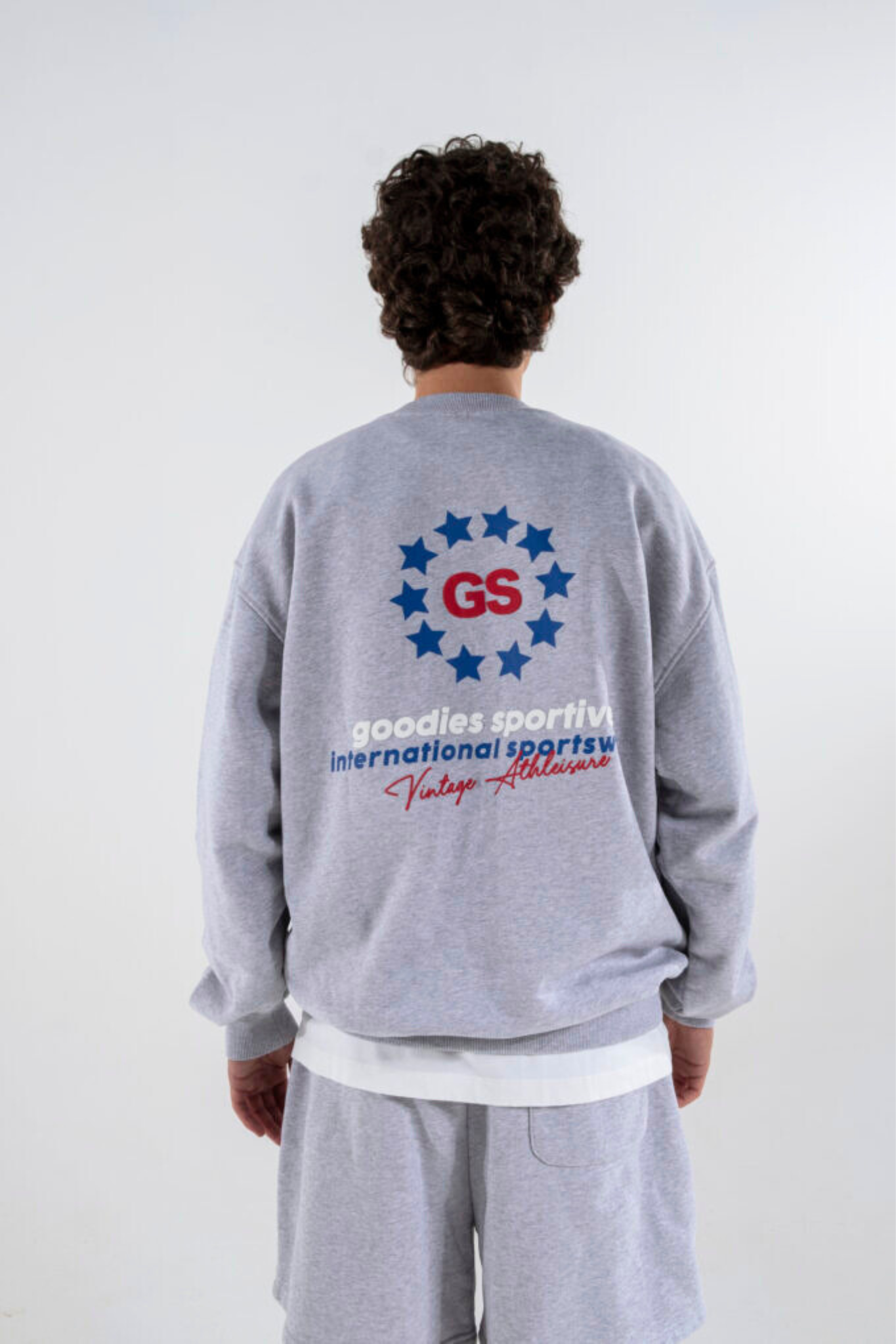 Model wearing the Goodies Sportive imperial premium crewneck in grey and grahpic in red and blue. Back view