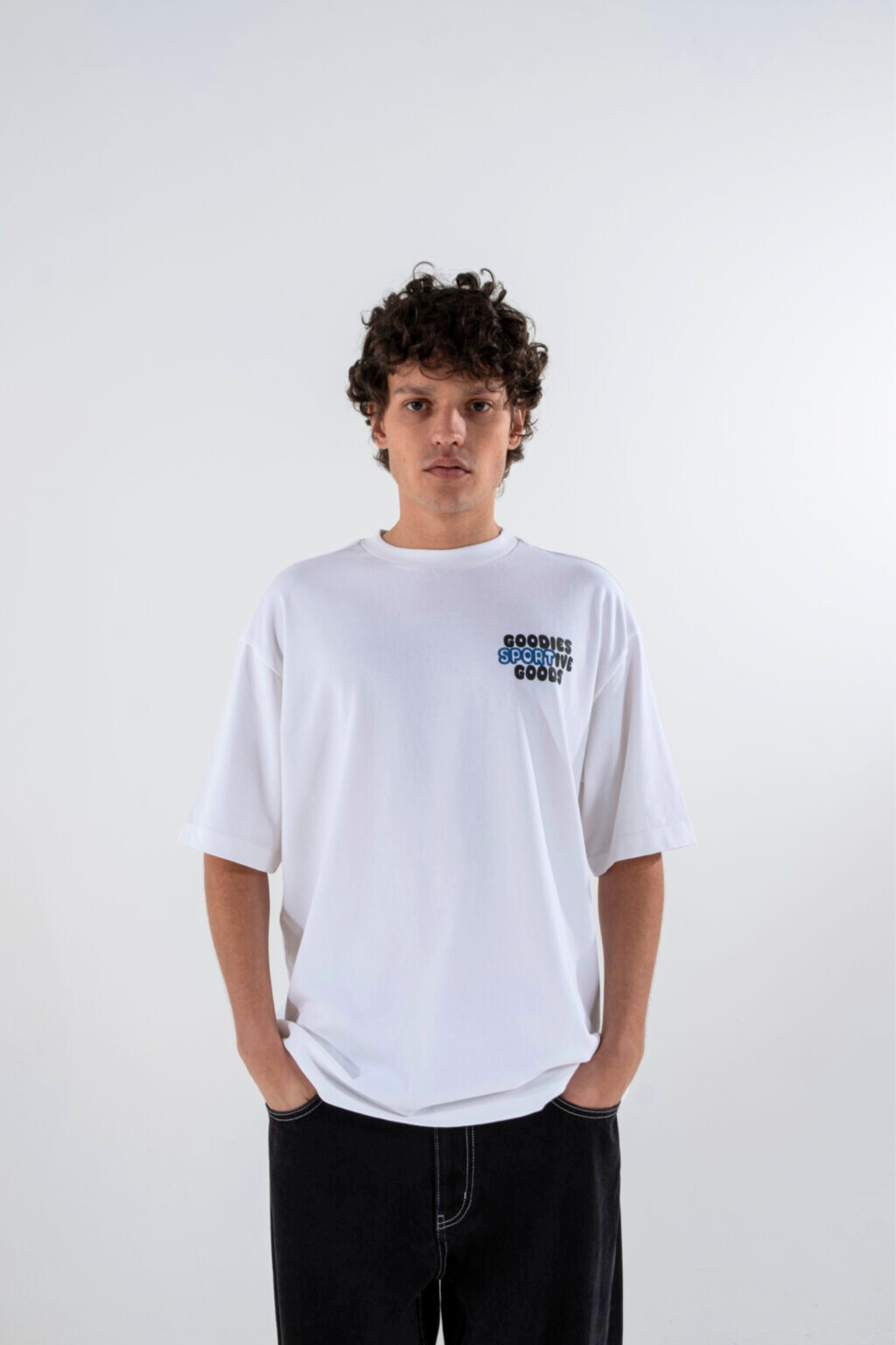 Model wearing the Goodies Sportive goods t-shirt in white and graphic in black and blue. Front view