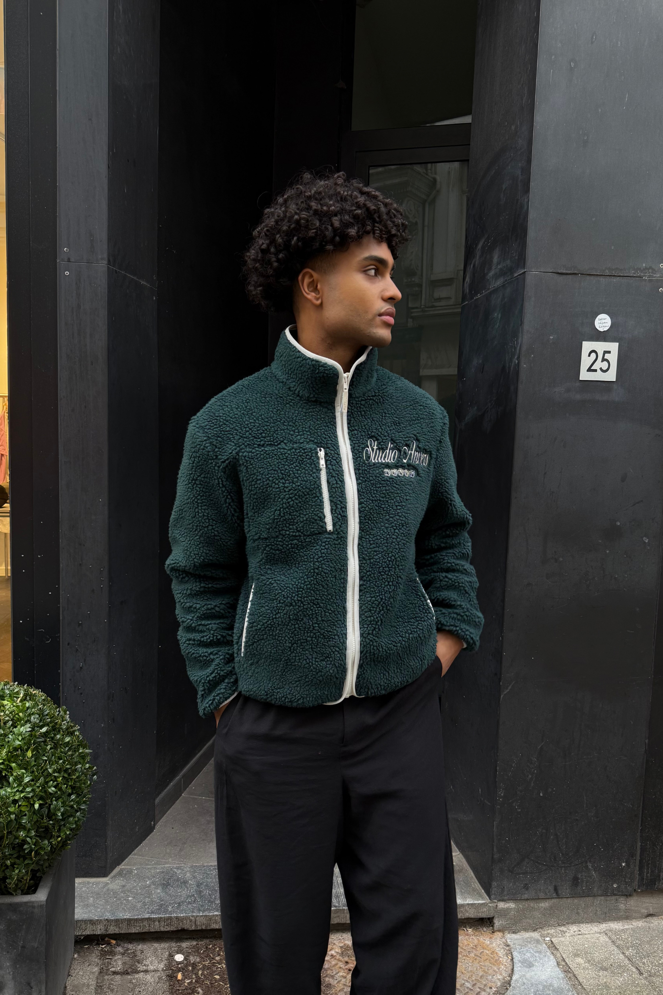 Model wearing the Studio Anvers lucky sherpa sweater in green and logo in white. Front view