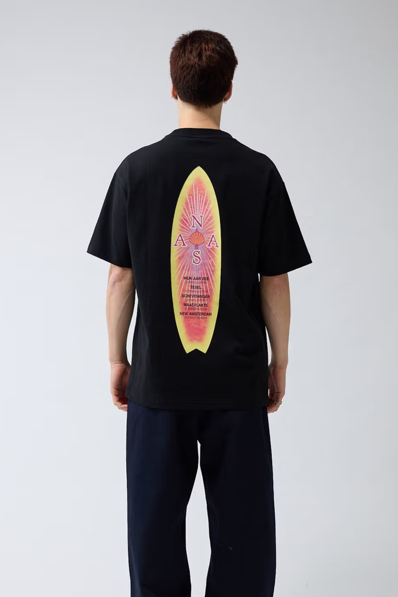 Model wearing the New Amsterdam surfboard t-shirt in black and graphic in red and yellow. Back view