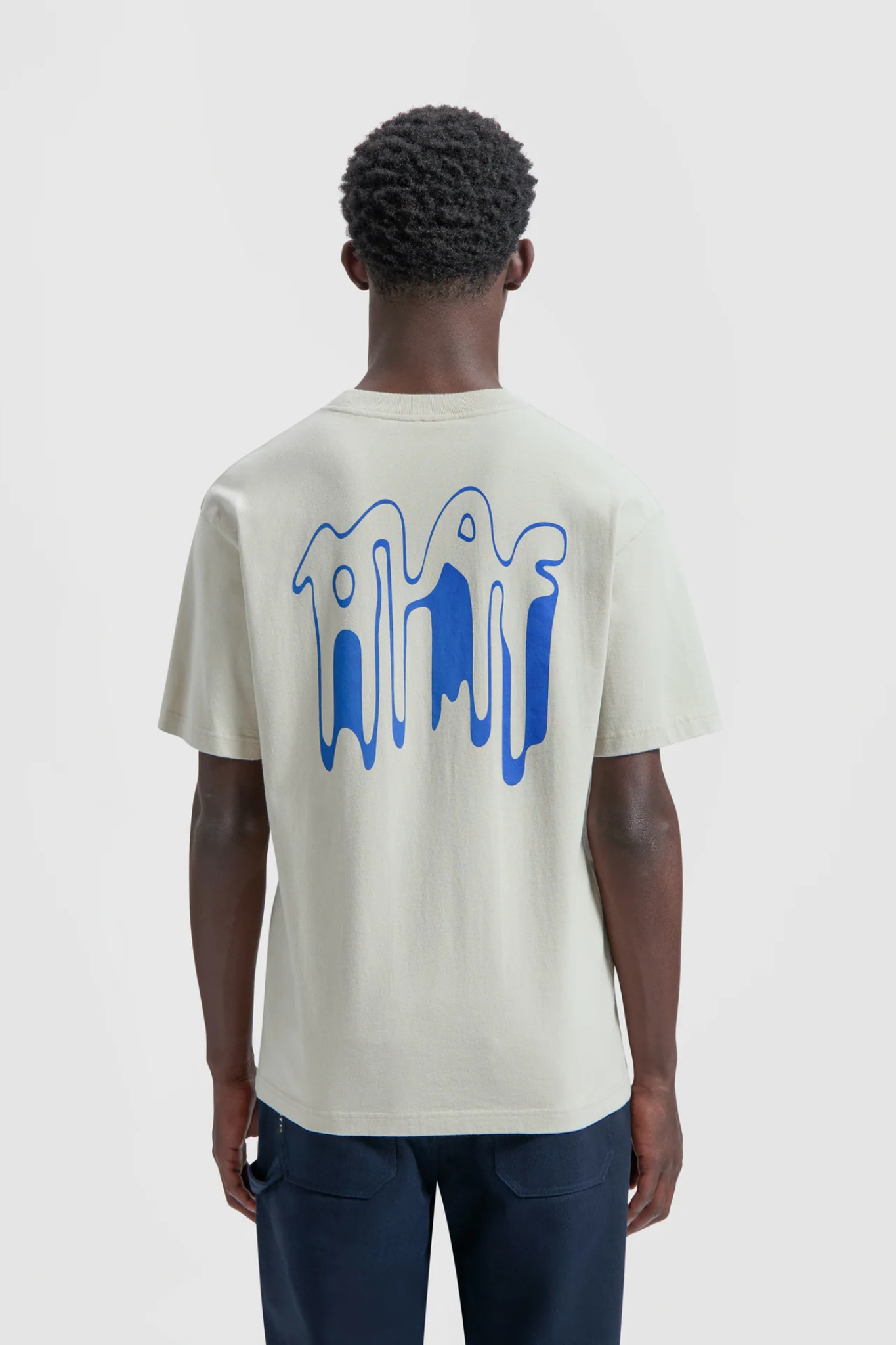 Model wearing the Olaf smudge logo t-shirt in beige and logo in blue. Back view