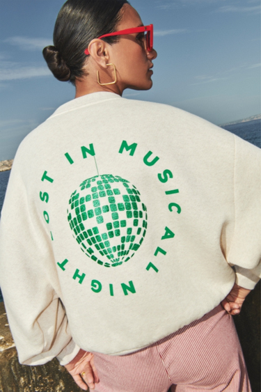 Model wearing the By-Bar bibi disco sweater in beige with letters in green. Back view