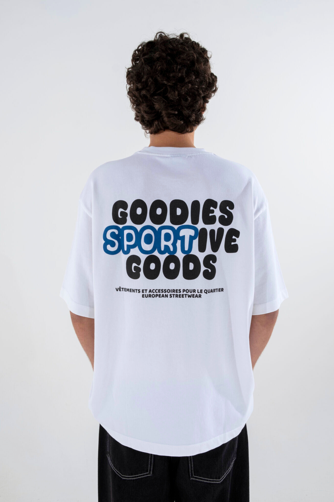 Model wearing the Goodies Sportive goods t-shirt in white and graphic in black and blue. Back view