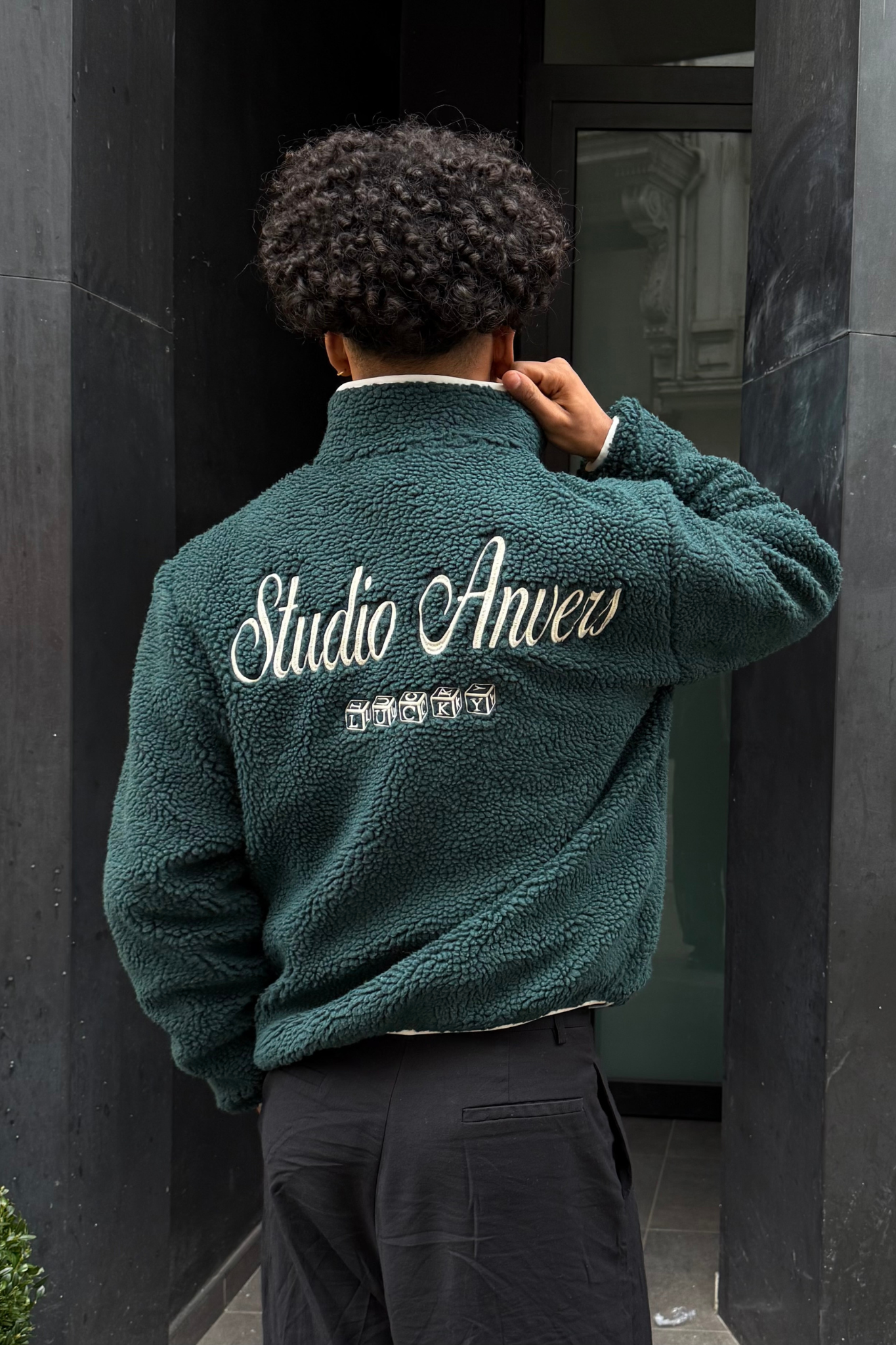 Model wearing the Studio Anvers lucky sherpa sweater in green and logo in white. Back view