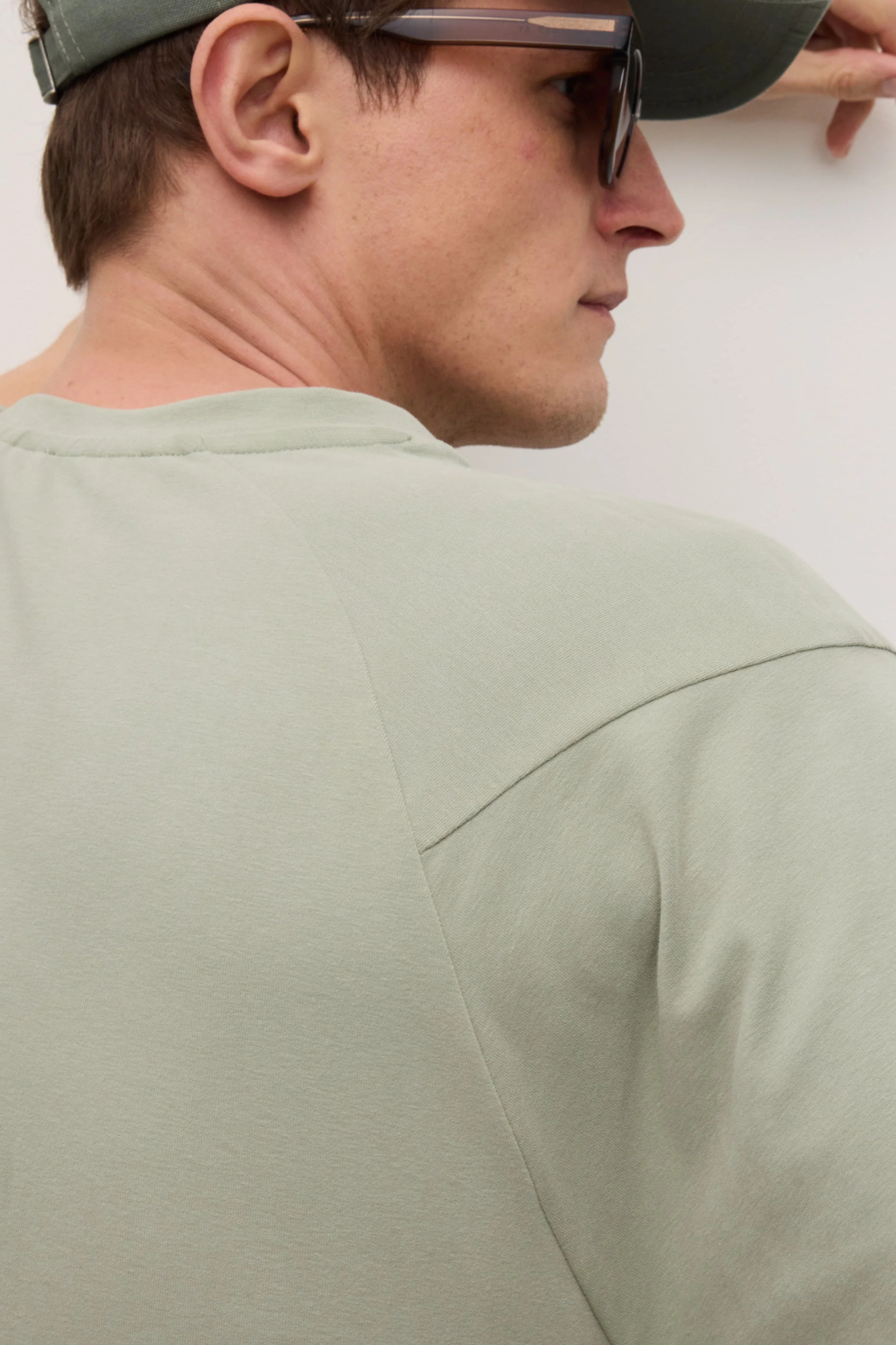 Model wearing the Goodpeople ted t-shirt in faded green. Back view