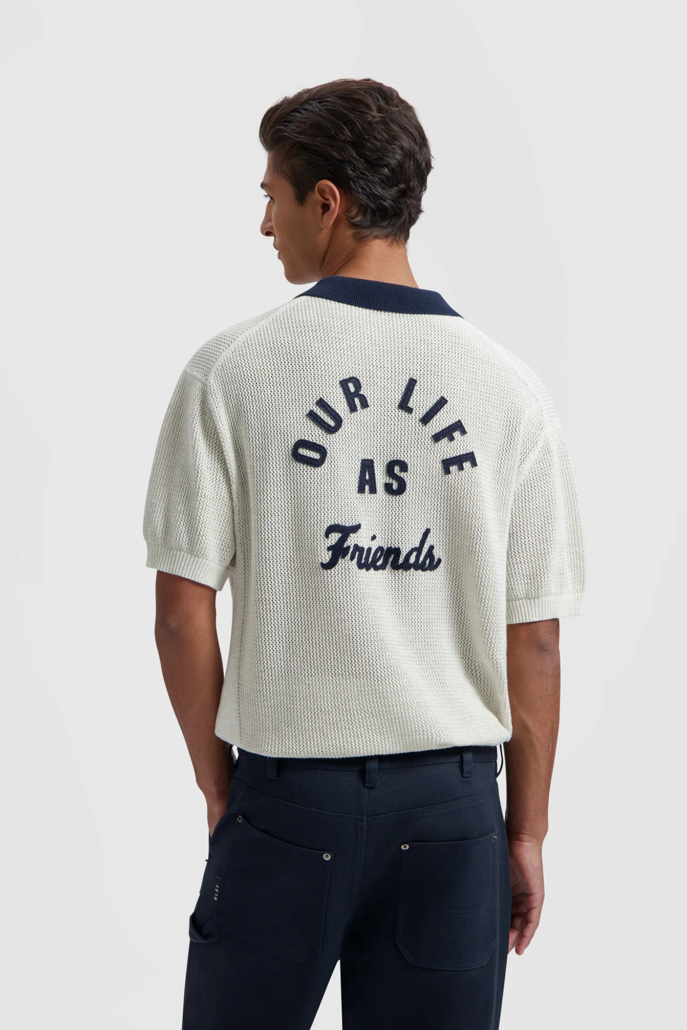 Model wearing the Olaf varsity polo knit in off white and text in dark blue. Back view