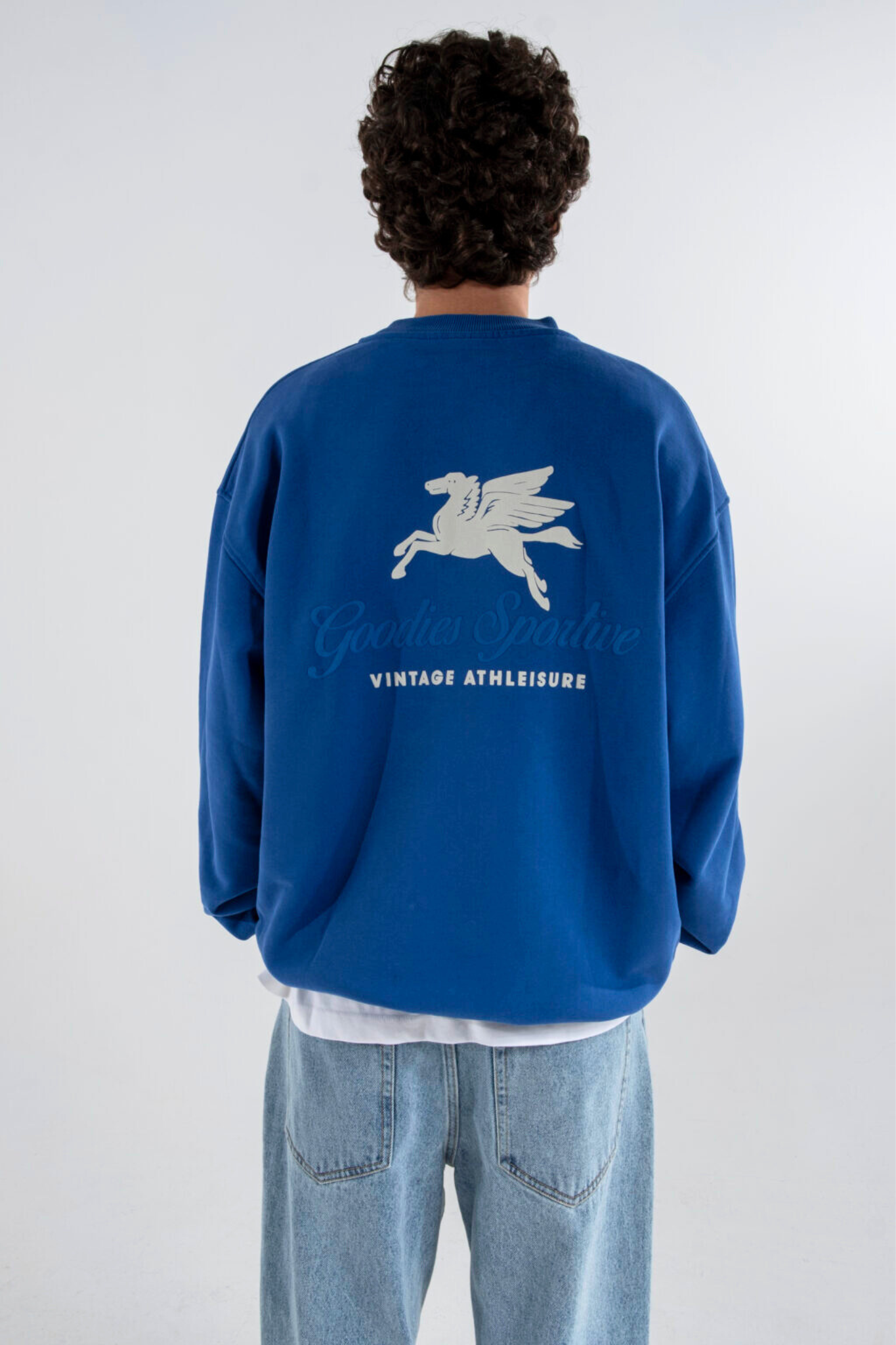 Model wearing the Goodies Sportive crewneck sweater in blue and logo in white. Back view