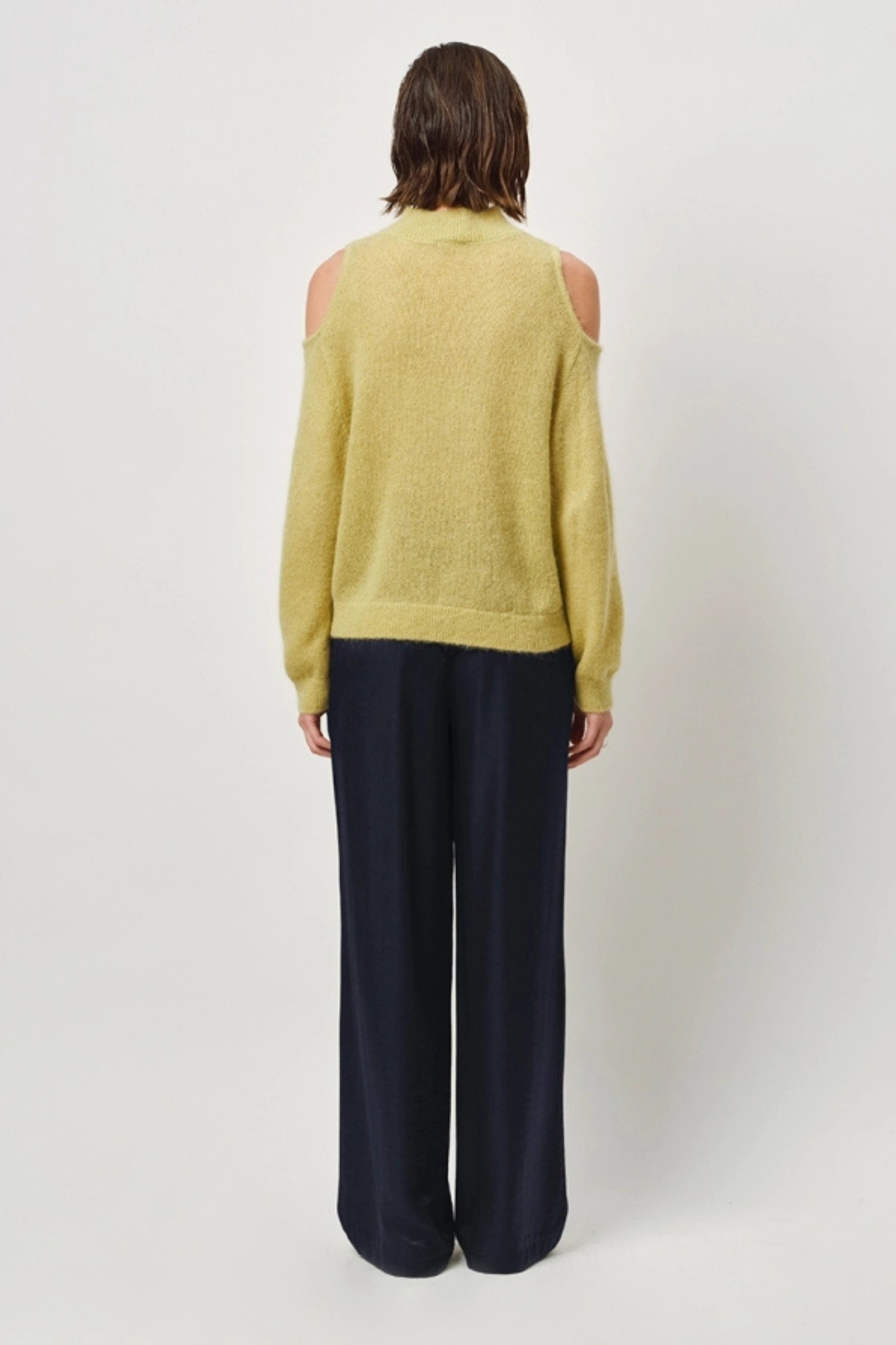 Model wearing the Dante6 aviel open shoulder sweater in lemon grass. Back view