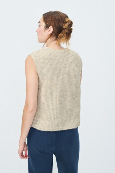 Model wearing the American Vintage beige sleeveless cardigan with logo in blue. Back view