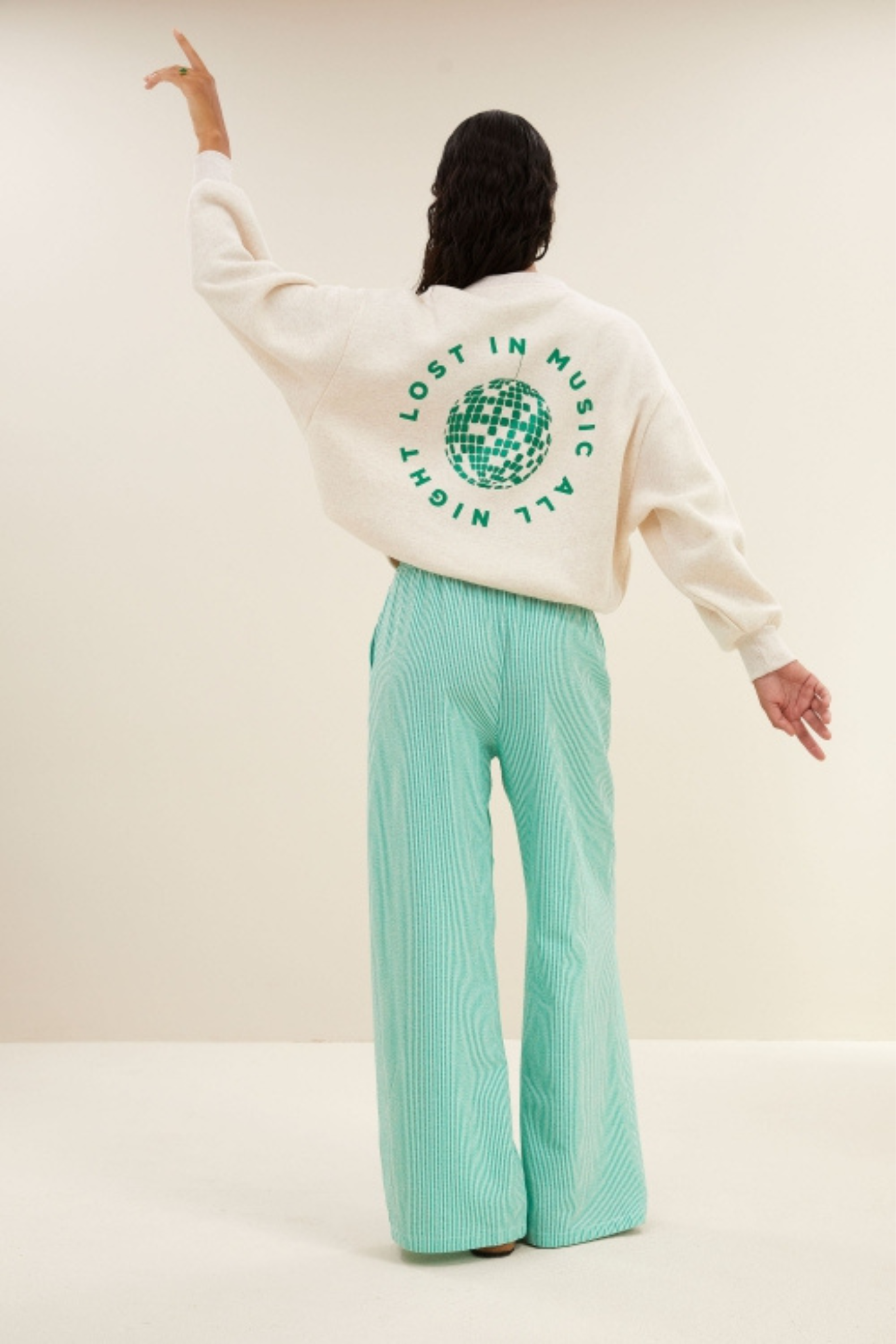 Model wearing the By-Bar bibi disco sweater in beige with letters in green. Back view