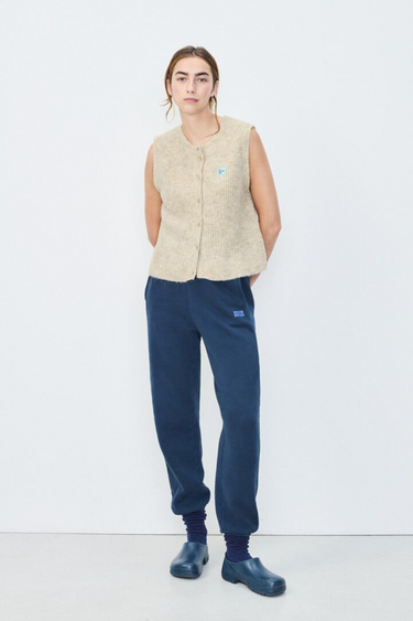 Model wearing the American Vintage beige sleeveless cardigan with logo in blue. Front view