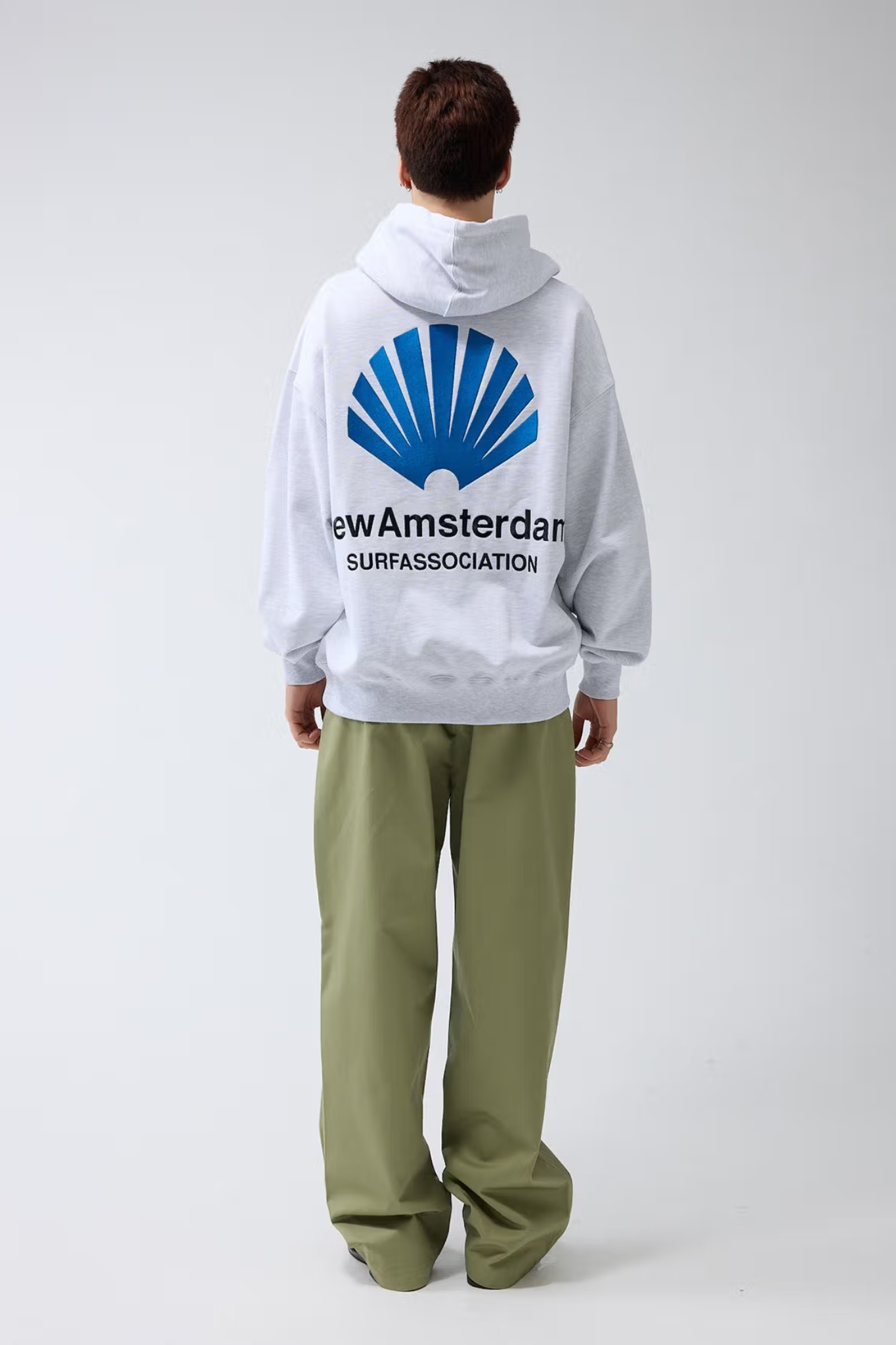 Model wearing the New Amsterdam light grey logo hoodie with logo in blue. Back view