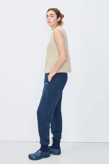 Model wearing the American Vintage beige sleeveless cardigan with logo in blue. Side view