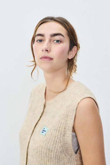 Model wearing the American Vintage beige sleeveless cardigan with logo in blue. Side view